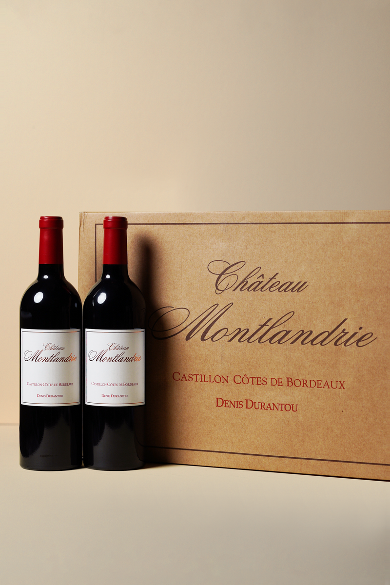 Two bottles of Chateau Montlandrie wine in front of a branded wooden box on a beige background